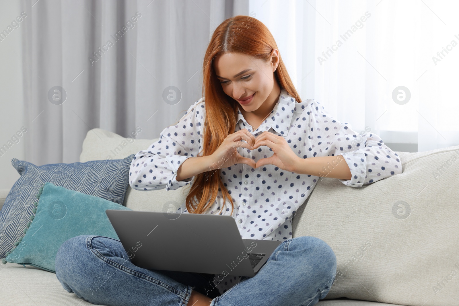 Photo of Woman making heart with hands during video chat via laptop at home. Long-distance relationship