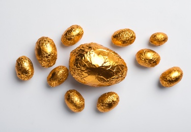 Chocolate eggs wrapped in golden foil on white background, flat lay