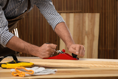 Carpenter working with timber at table indoors, closeup