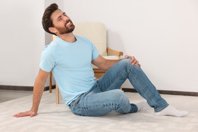 Photo of Man touching knee on white carpet near armchair at home