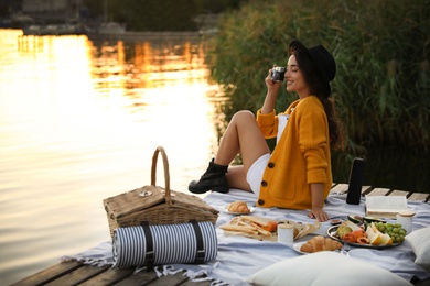 Photo of Young woman taking picture with camera on pier at picnic