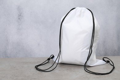 Photo of White drawstring bag on grey textured table. Space for text