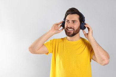 Happy man listening music with headphones on light grey background. Space for text