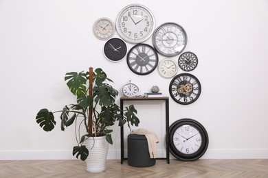 Photo of Console table, beautiful houseplant and collection of different clocks on white wall in room