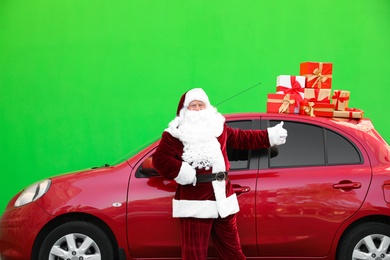 Photo of Authentic Santa Claus near car with presents on roof against green background