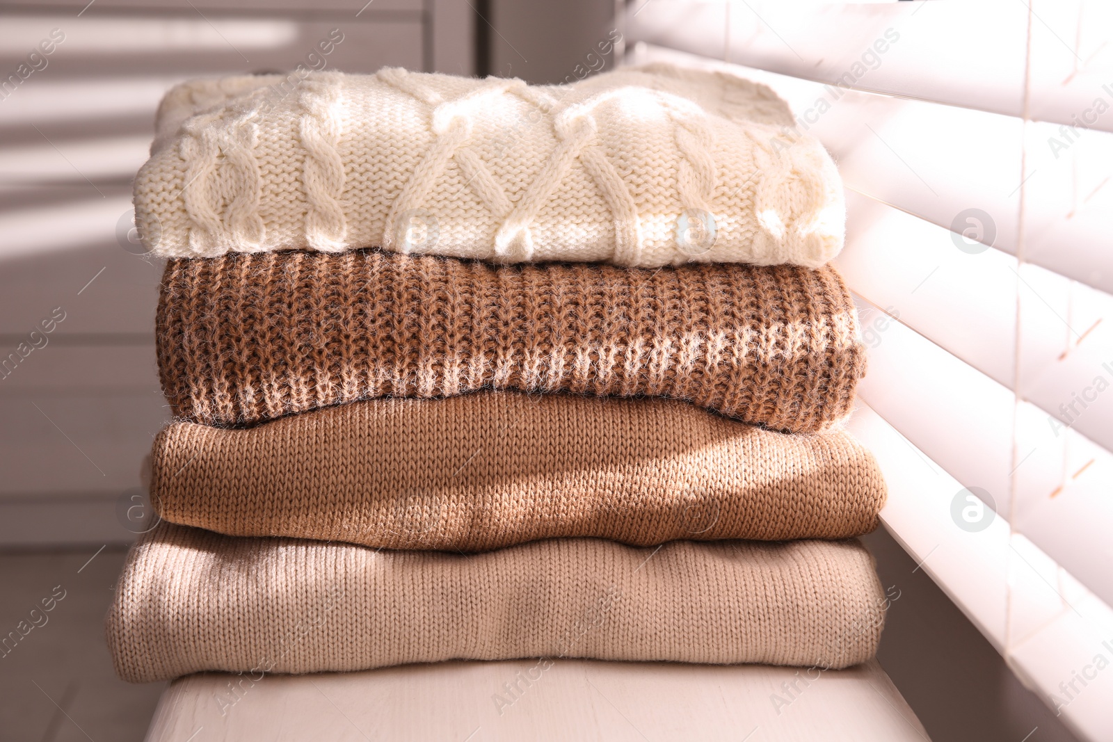 Photo of Stack of folded warm sweaters on window sill indoors, closeup