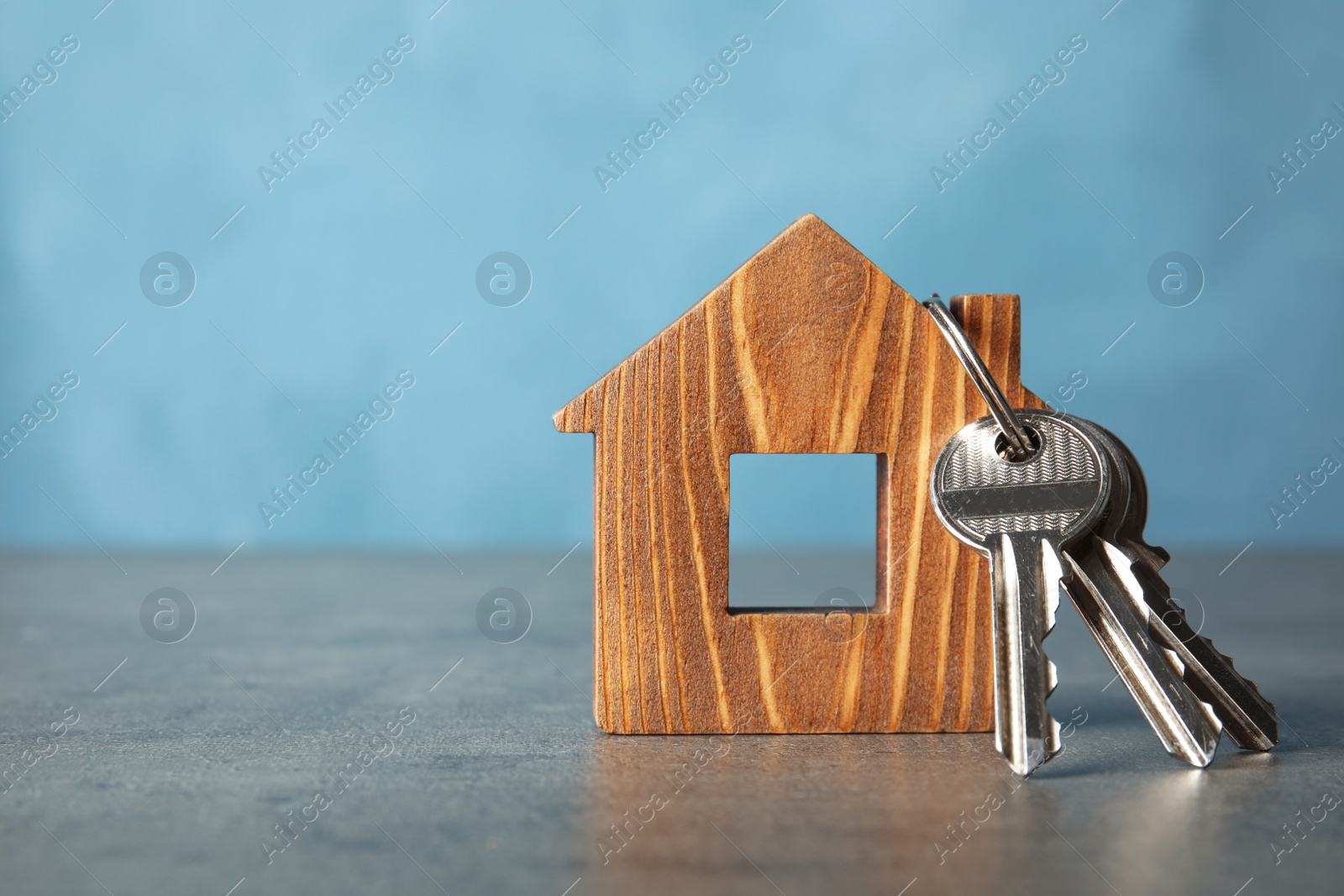 Photo of Bunch of keys and house model on table against color background. Space for text