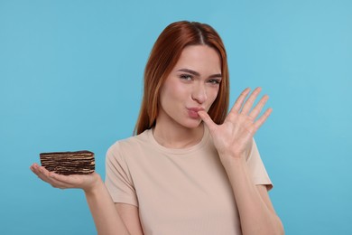 Photo of Young woman with tasty cake on light blue background