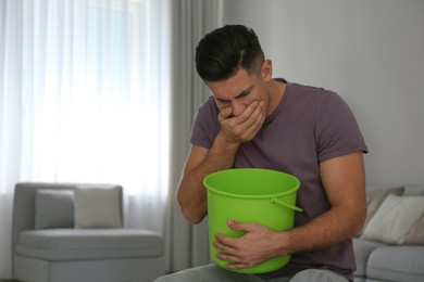Photo of Man with bucket suffering from nausea at home, space for text. Food poisoning