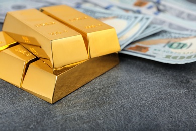 Photo of Stacked gold bars and dollar bills on table, closeup. Space for text