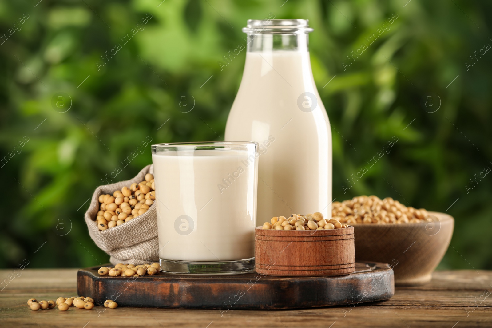 Photo of Fresh soy milk and grains on white wooden table against blurred background