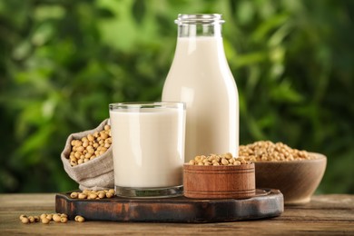 Fresh soy milk and grains on white wooden table against blurred background