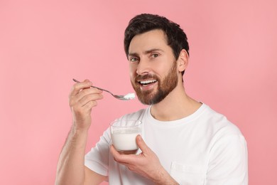 Photo of Happy man with delicious yogurt and spoon on pink background