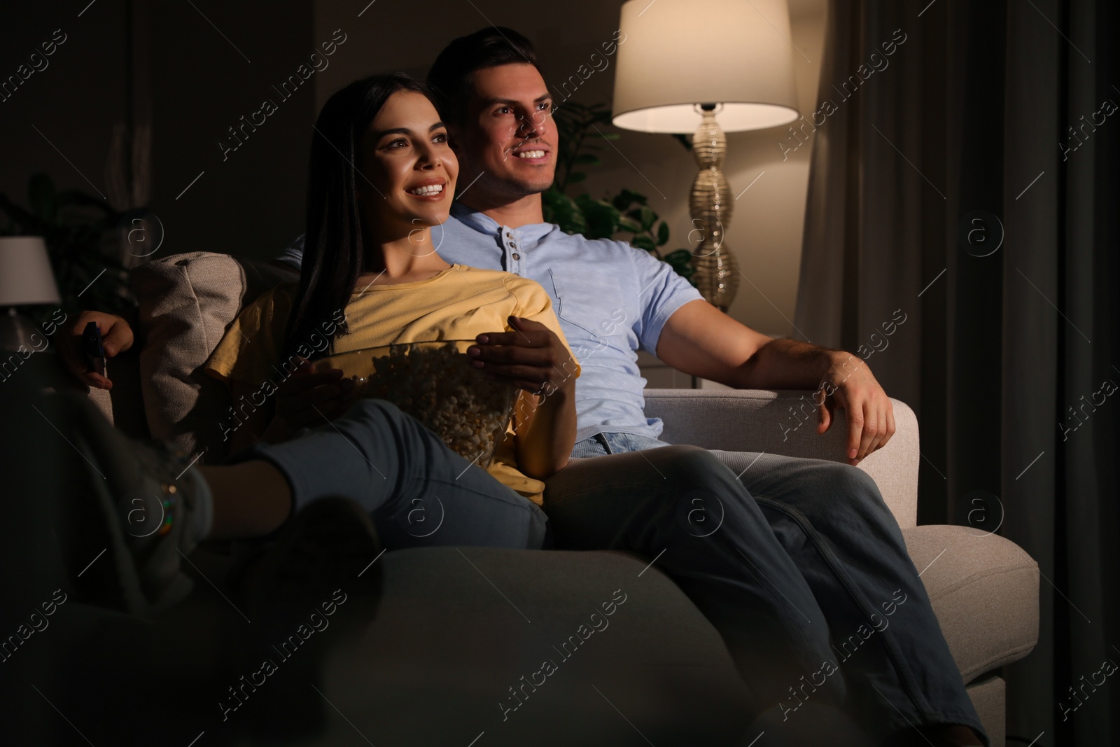 Photo of Couple watching movie with popcorn on sofa at night