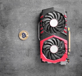 Modern video card and bitcoin on grey table, top view