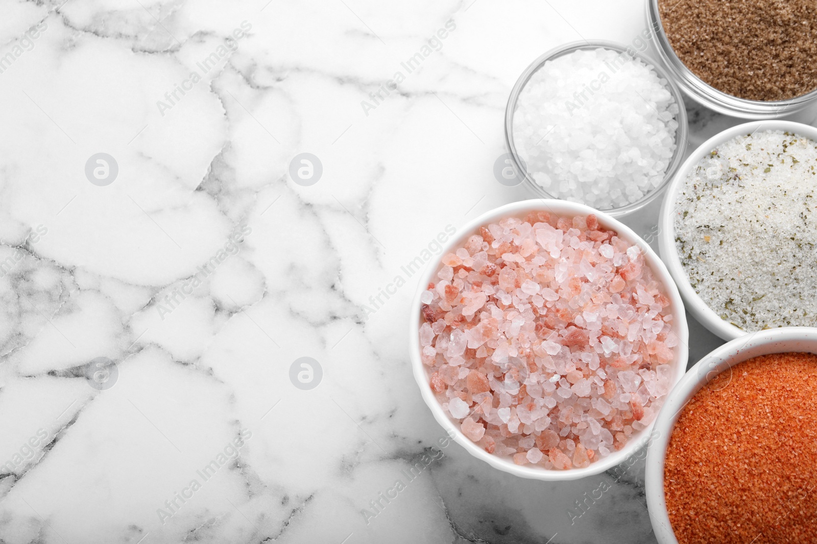 Photo of Different kinds of salt on white marble table, flat lay. Space for text