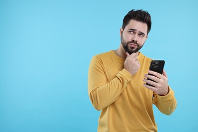 Photo of Young man using smartphone on light blue background, space for text
