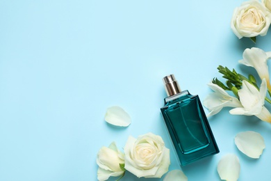 Photo of Flat lay composition with bottle of perfume and flowers on light blue background, space for text