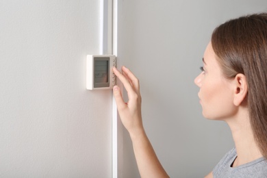 Photo of Woman adjusting thermostat on white wall. Heating system