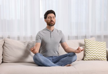 Photo of Man meditating on sofa at home. Harmony and zen
