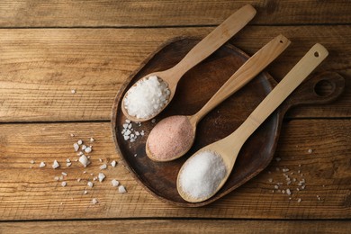 Photo of Different natural salt in spoons on wooden table, flat lay. Space for text