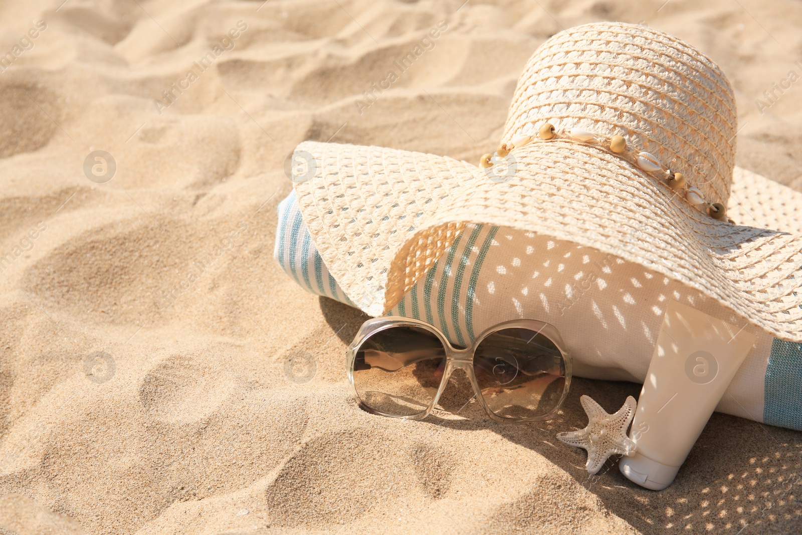 Photo of Straw hat, towel, sunscreen, starfish and sunglasses on sand. Space for text