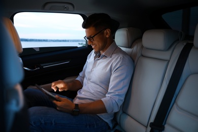 Photo of Handsome man using tablet on backseat of modern car