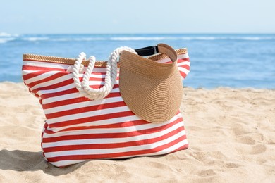 Photo of Stylish striped bag with visor cap on sandy beach near sea