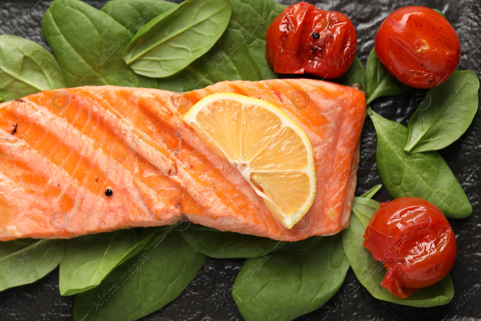 Photo of Tasty grilled salmon with tomatoes, spinach and lemon on table, top view