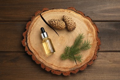 Pine essential oil, cones and twig on wooden table, top view