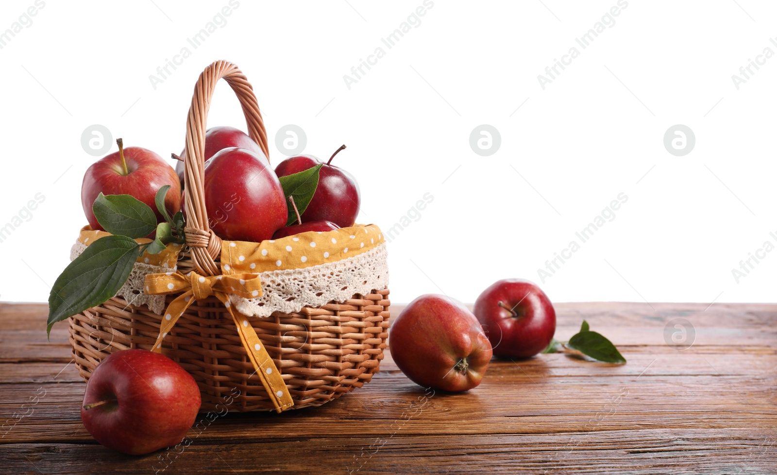 Photo of Ripe red apples in wicker basket on wooden table against white background. Space for text