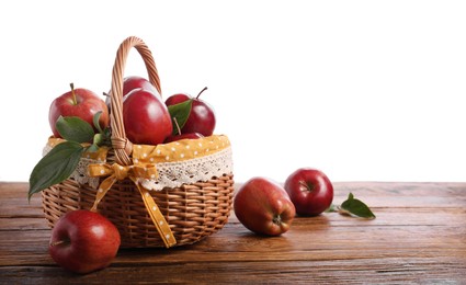 Photo of Ripe red apples in wicker basket on wooden table against white background. Space for text