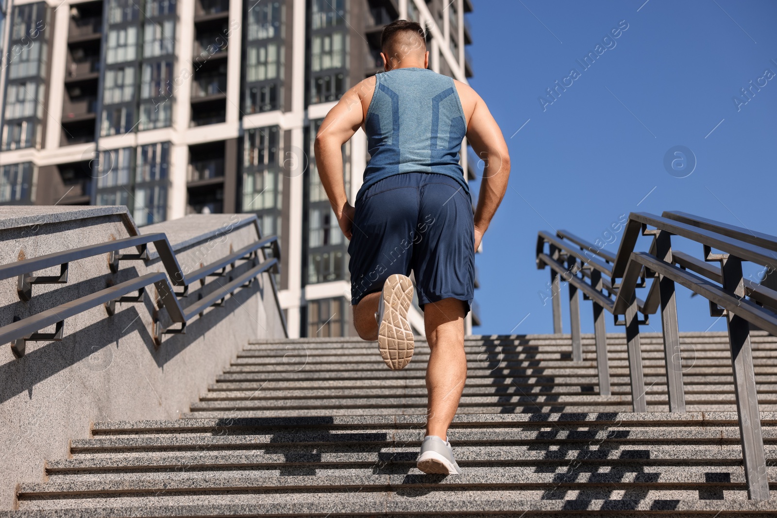 Photo of Man running up stairs outdoors on sunny day, back view