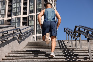 Photo of Man running up stairs outdoors on sunny day, back view