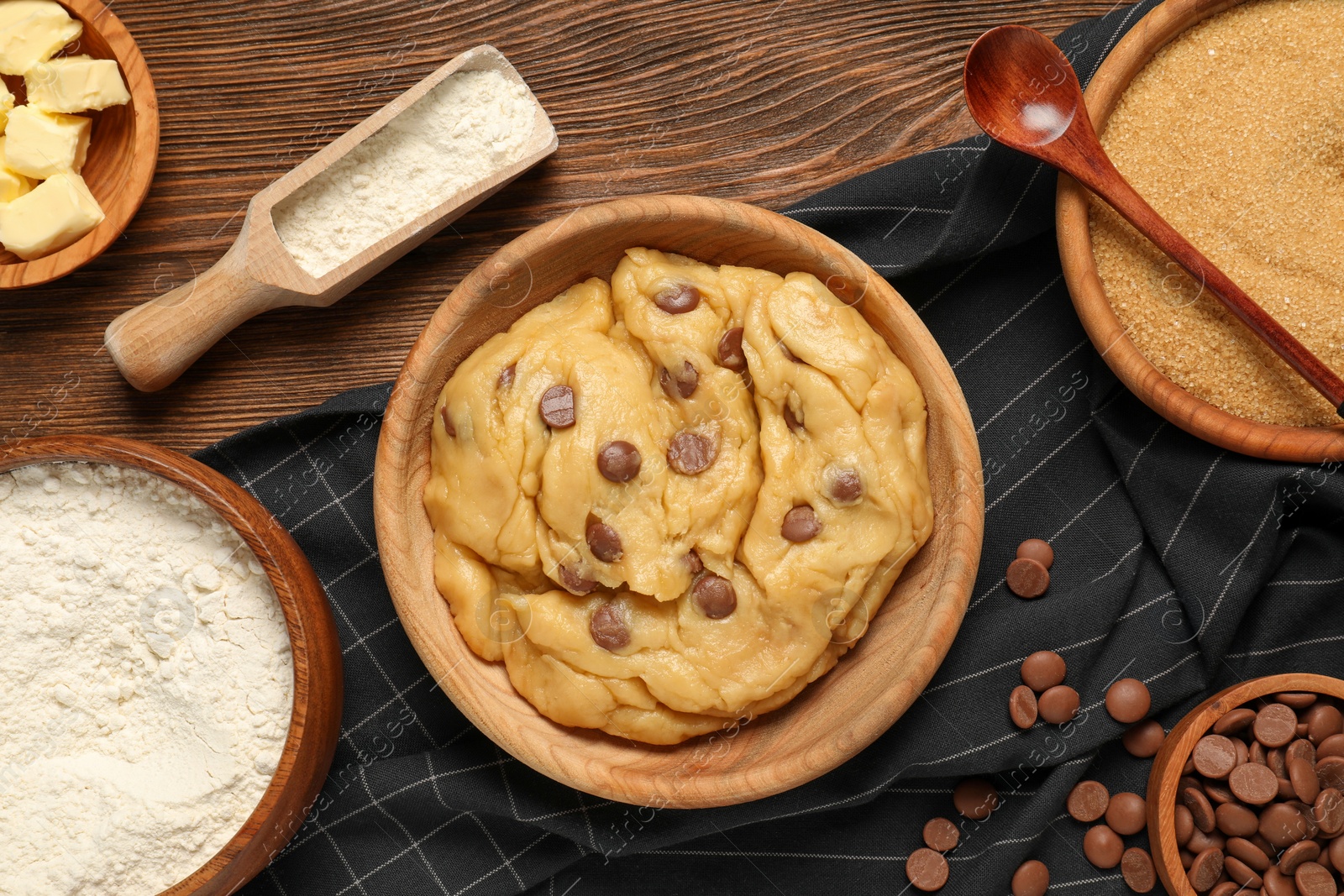 Photo of Fresh dough and different ingredients for cooking chocolate chip cookies on wooden table, flat lay