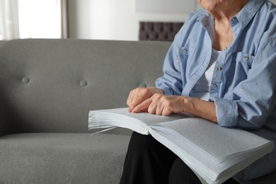 Blind senior person reading book written in Braille on sofa indoors, closeup. Space for text