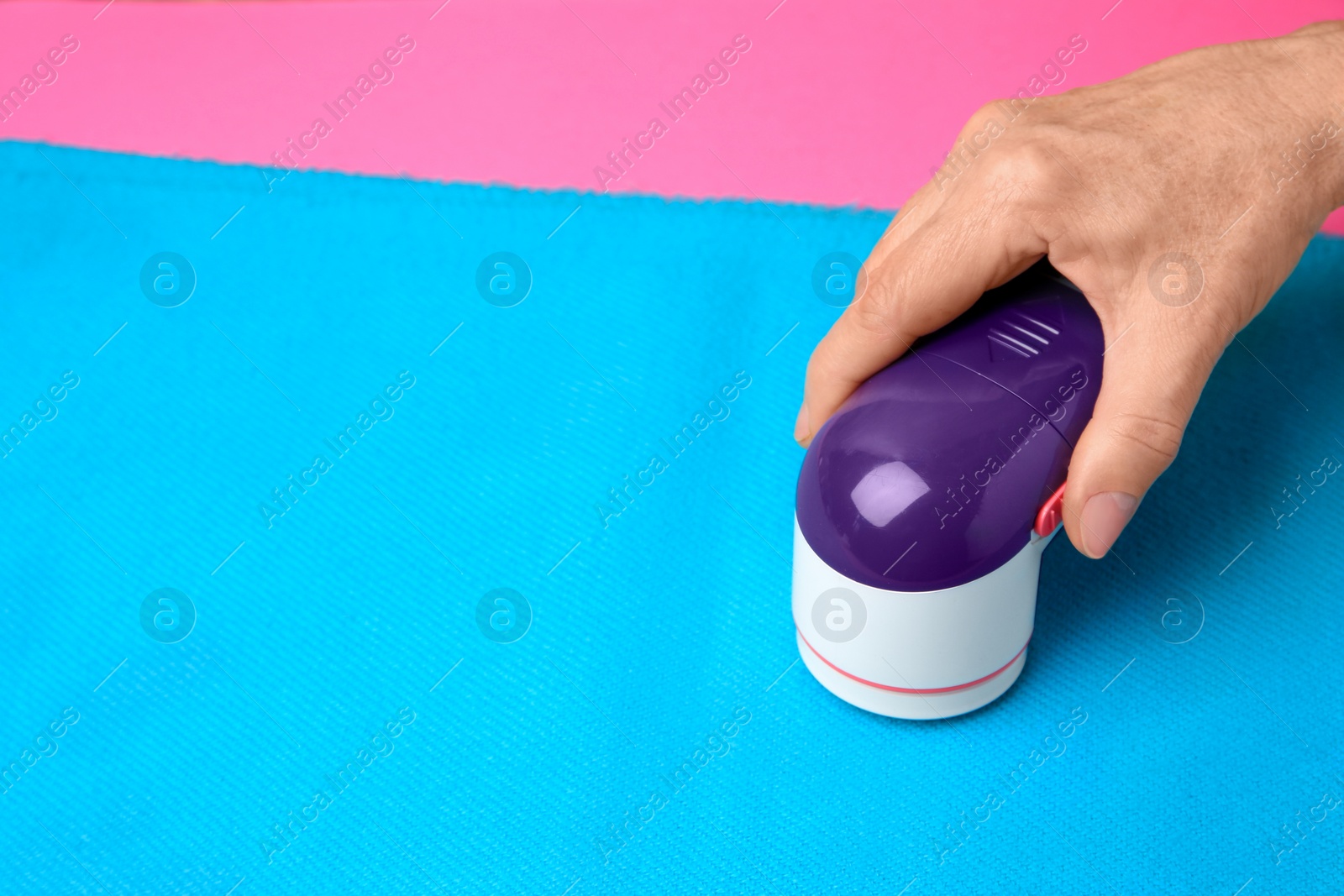 Photo of Woman cleaning light blue scarf with fabric shaver on pink background, closeup