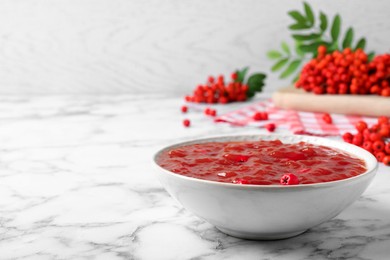 Delicious rowan jam in bowl and berries on white marble table. Space for text