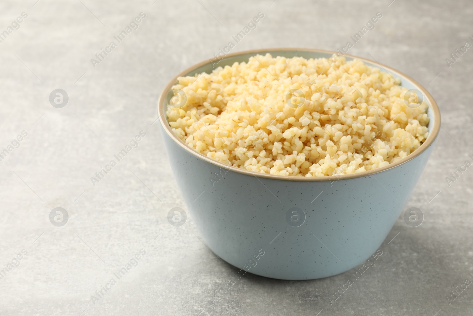 Photo of Delicious bulgur in bowl on light grey table, closeup. Space for text