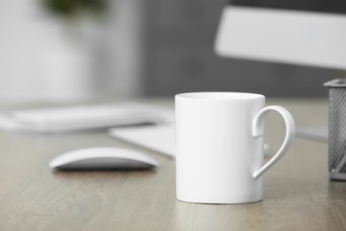 Photo of White ceramic mug on wooden table at workplace. Mockup for design