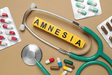 Photo of Yellow cubes with word Amnesia, stethoscope and pills on light brown background, flat lay
