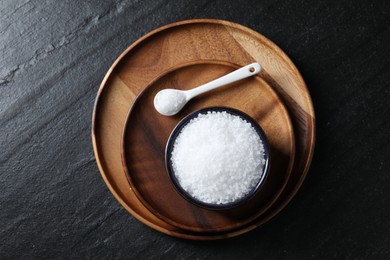 Photo of Organic white salt in bowl and spoon on black table, top view