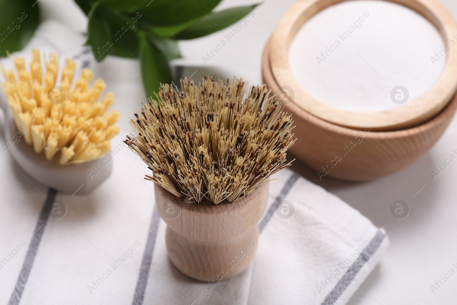 Photo of Cleaning brushes, baking soda and green leaves on white table, closeup