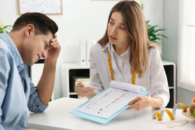 Photo of Young nutritionist consulting patient at table in clinic