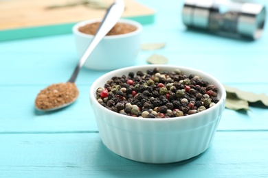 Bowl of mixed pepper corns on blue wooden table, space for text