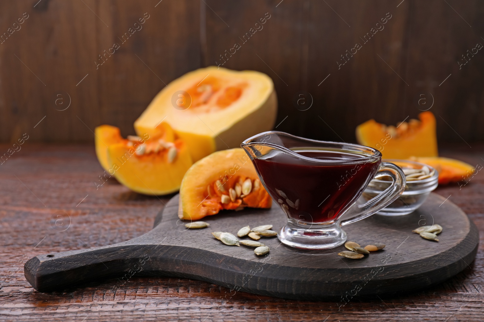 Photo of Fresh pumpkin seed oil in glass sauceboat on wooden table. Space for text