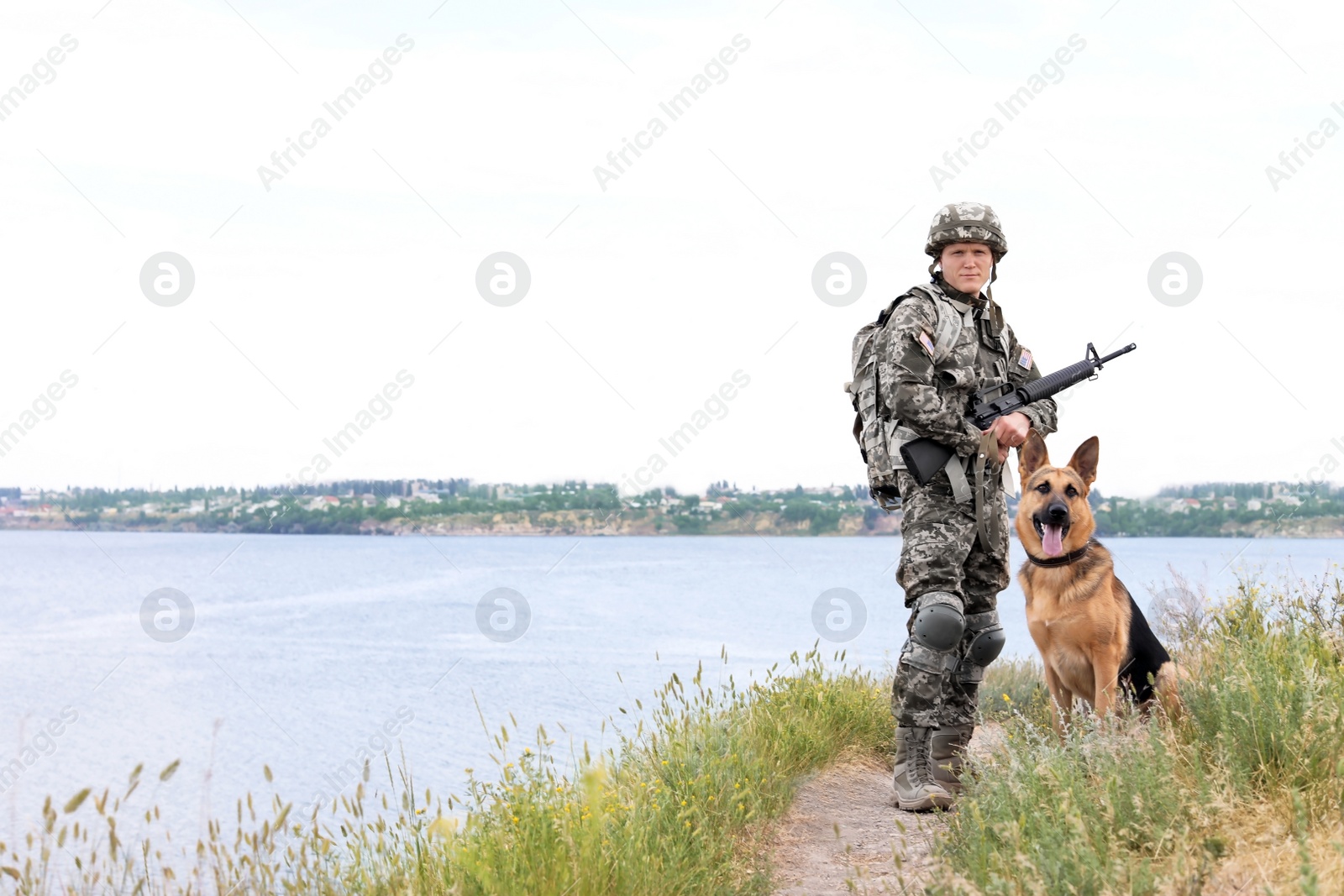 Photo of Man in military uniform with German shepherd dog near river