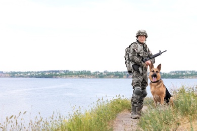 Man in military uniform with German shepherd dog near river