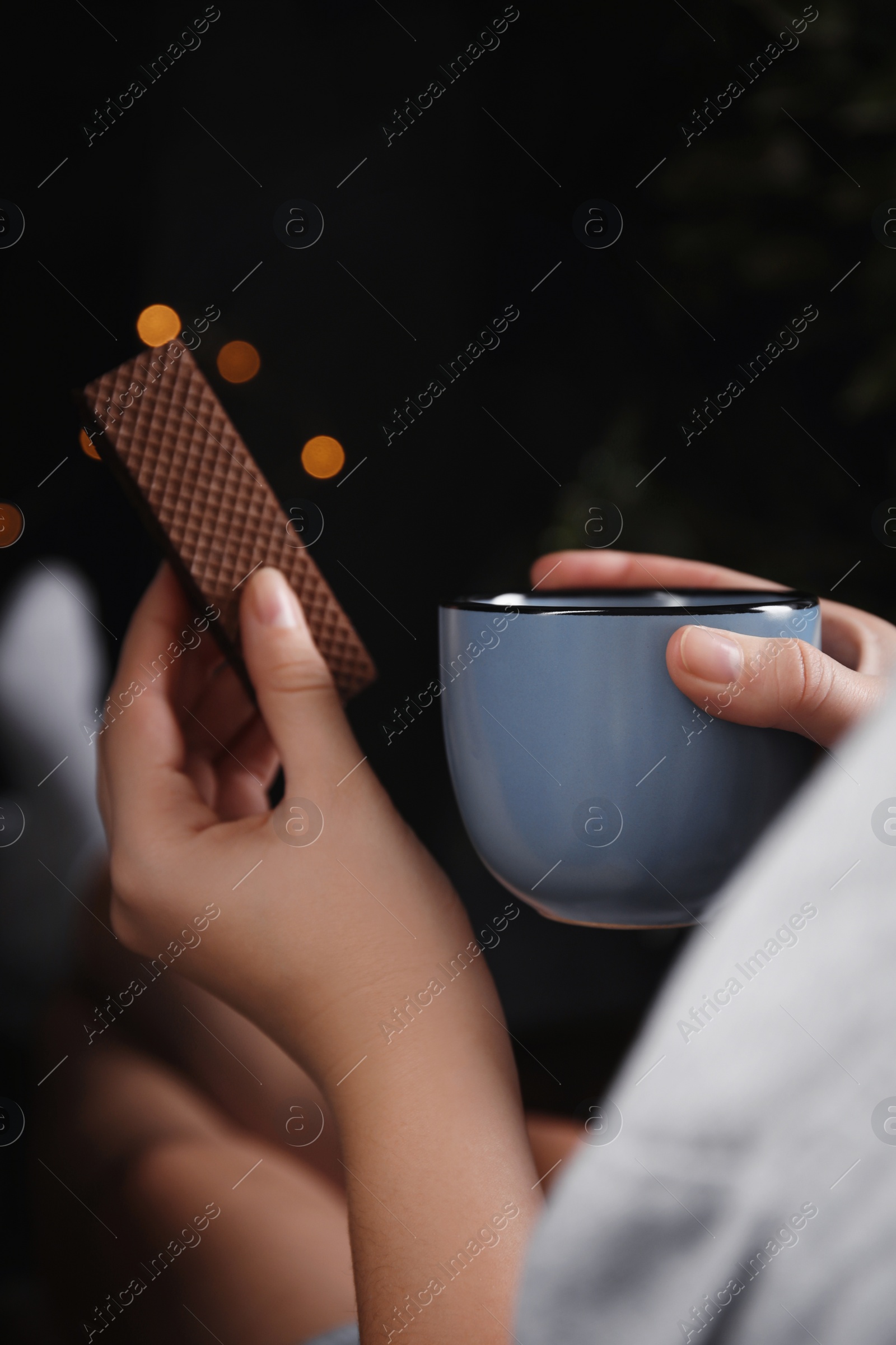 Photo of Woman with wafer and coffee on dark background, closeup. Early breakfast