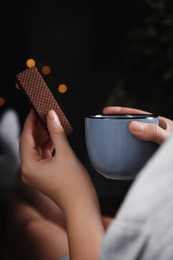 Woman with wafer and coffee on dark background, closeup. Early breakfast